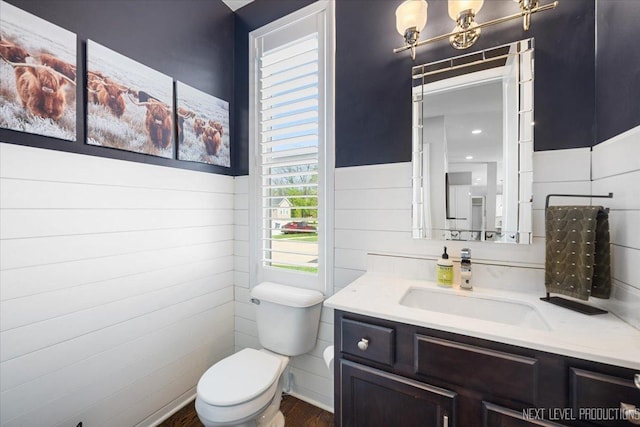 half bathroom with toilet, wood finished floors, vanity, and a wainscoted wall
