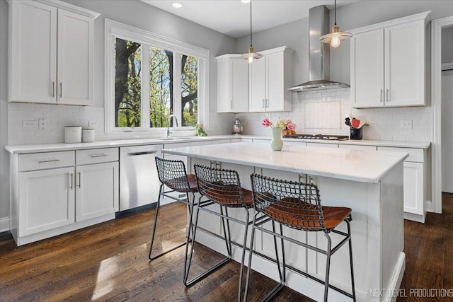 kitchen featuring wall chimney range hood, stainless steel dishwasher, a kitchen breakfast bar, white cabinetry, and recessed lighting