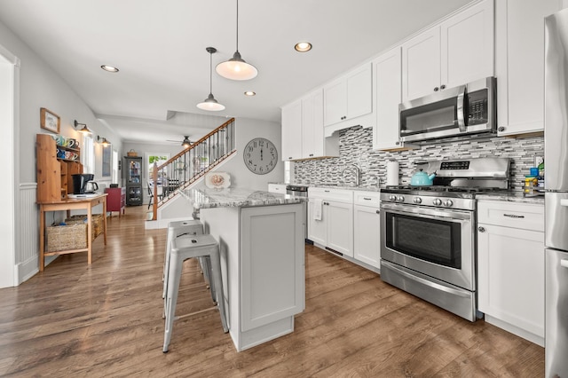 kitchen with stainless steel appliances, tasteful backsplash, white cabinets, a center island, and a sink