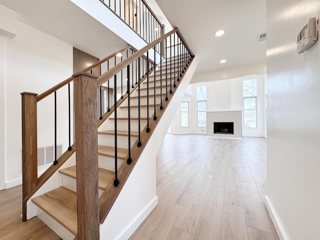 stairway featuring baseboards, wood finished floors, recessed lighting, and a tiled fireplace
