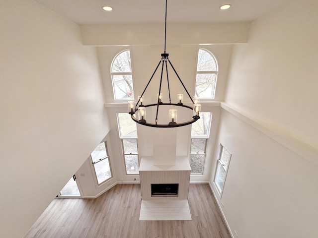 unfurnished living room with a chandelier, a high ceiling, light wood finished floors, baseboards, and recessed lighting