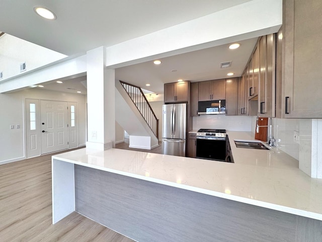 kitchen featuring appliances with stainless steel finishes, light wood-type flooring, a sink, a peninsula, and recessed lighting