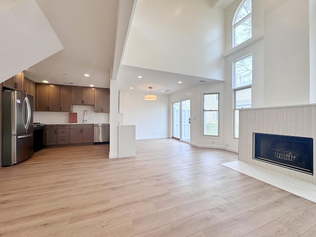 unfurnished living room featuring a high ceiling, a sink, light wood-type flooring, recessed lighting, and a tile fireplace