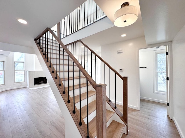 stairway featuring baseboards, wood finished floors, healthy amount of natural light, and recessed lighting