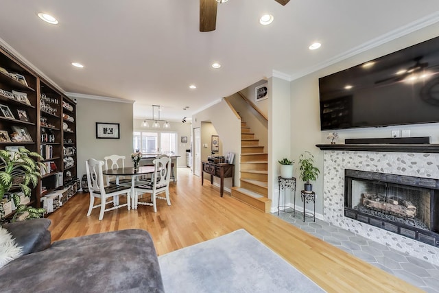 living room featuring crown molding, ceiling fan, wood finished floors, stairway, and a tiled fireplace