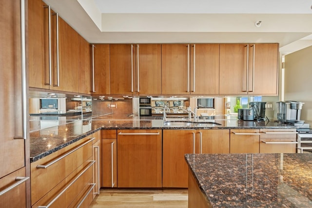 132 E Delaware Pl Unit 4901, Chicago, IL 60611 - kitchen with a sink, dark stone countertops, brown cabinetry, light wood finished floors, and stainless steel oven