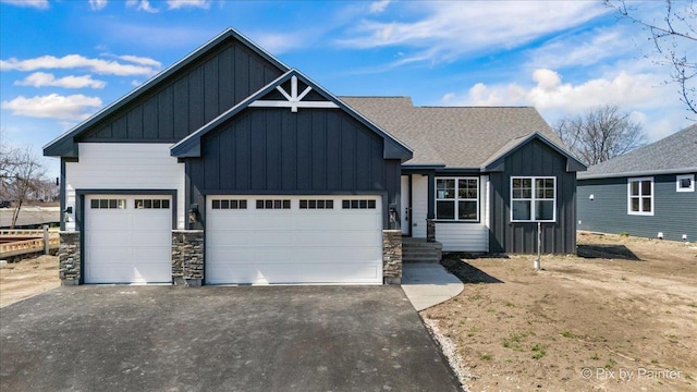 view of front facade featuring board and batten siding, driveway, an attached garage, stone siding, and roof with shingles