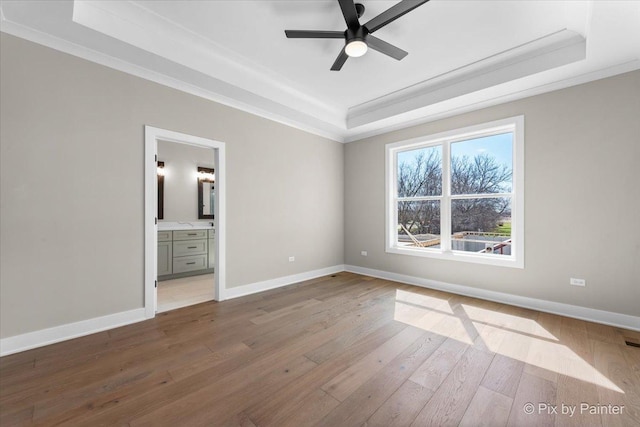 unfurnished bedroom featuring a raised ceiling, baseboards, hardwood / wood-style floors, ornamental molding, and ensuite bathroom