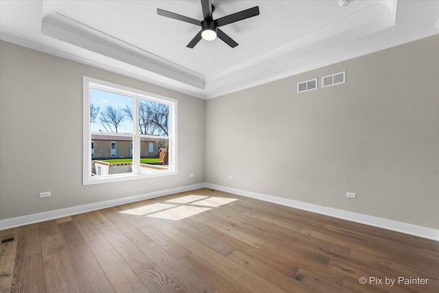 unfurnished room featuring a raised ceiling, wood-type flooring, baseboards, ceiling fan, and ornamental molding