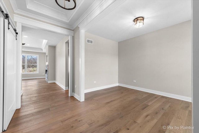 spare room with a barn door, wood finished floors, crown molding, and baseboards