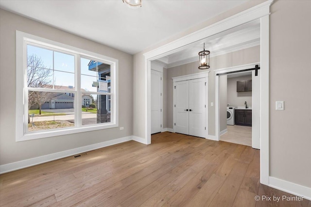 empty room with washer / dryer, baseboards, a barn door, and light wood-style flooring