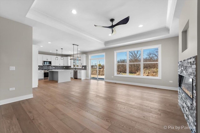 unfurnished living room featuring a tray ceiling, a ceiling fan, a glass covered fireplace, light wood finished floors, and recessed lighting