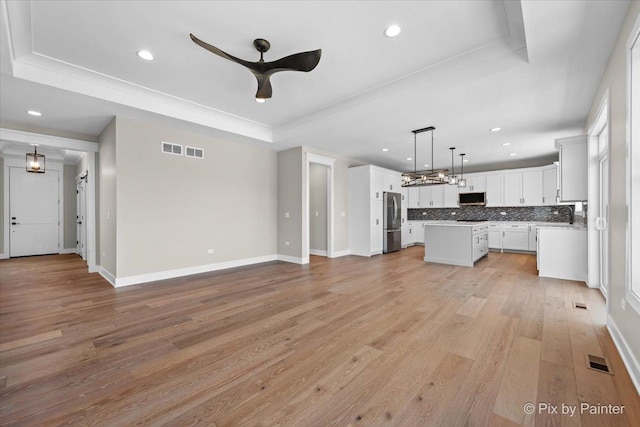 unfurnished living room with a tray ceiling, recessed lighting, a ceiling fan, light wood-type flooring, and baseboards