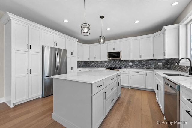 kitchen featuring appliances with stainless steel finishes, a sink, light wood finished floors, a kitchen island, and recessed lighting