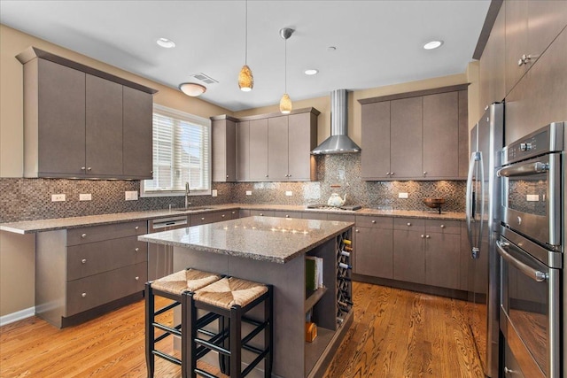 1147 Morgan St, Northbrook, IL 60062 - kitchen featuring wall chimney range hood, stainless steel appliances, light wood-style floors, a center island, and hanging light fixtures