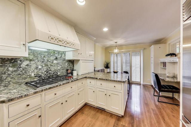 215 W Concord Ln, Chicago, IL 60614 - kitchen with a peninsula, a chandelier, under cabinet range hood, decorative backsplash, and stainless steel gas cooktop