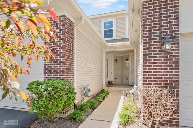 view of exterior entry with brick siding and a garage