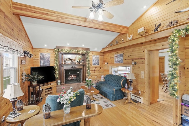 living room featuring wooden walls, wood finished floors, a lit fireplace, and a ceiling fan