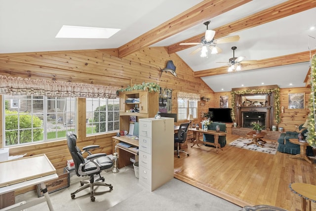 office area with wooden walls, a skylight, a fireplace with raised hearth, and a ceiling fan
