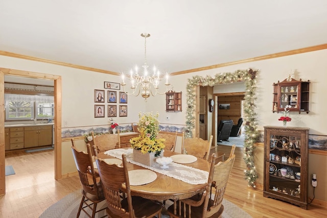 dining area with light wood-style floors, ornamental molding, a chandelier, and wainscoting