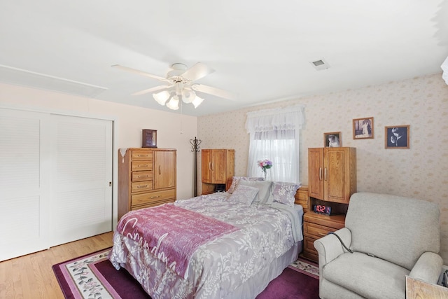 bedroom with a closet, wood finished floors, a ceiling fan, wallpapered walls, and attic access