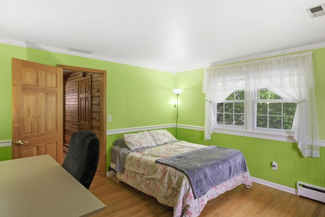 bedroom with baseboard heating, wainscoting, wood finished floors, crown molding, and wooden walls