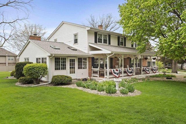 rear view of property with a chimney, a porch, a shingled roof, and a lawn