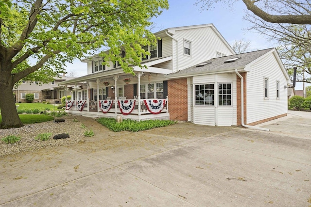 view of front of home featuring a porch, brick siding, concrete driveway, and a shingled roof