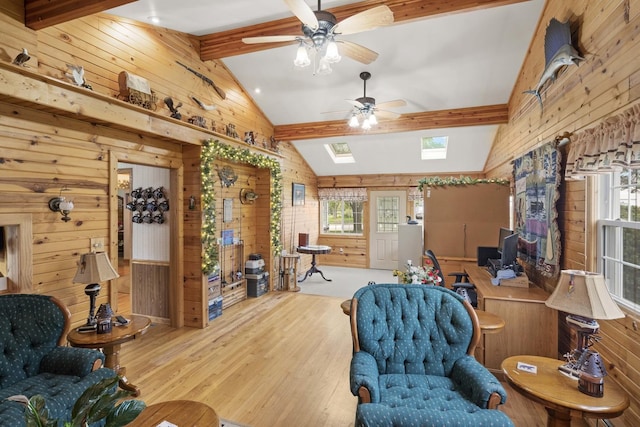 living area with wood walls, wood finished floors, a ceiling fan, and a skylight