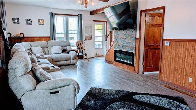 living room featuring wood finished floors, a wainscoted wall, wood walls, a ceiling fan, and a glass covered fireplace