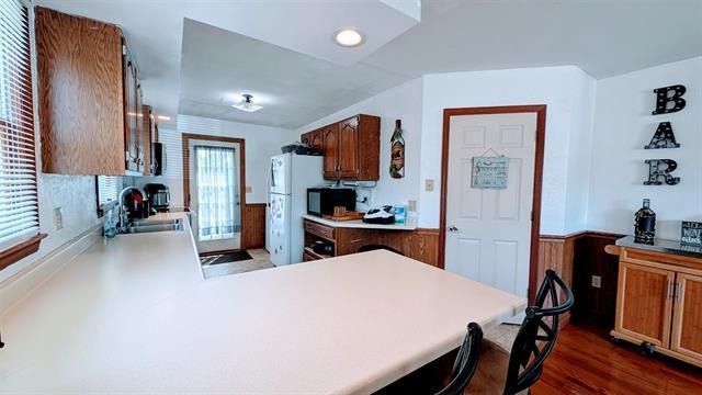 kitchen featuring a wainscoted wall, black microwave, dark wood-style floors, a sink, and light countertops