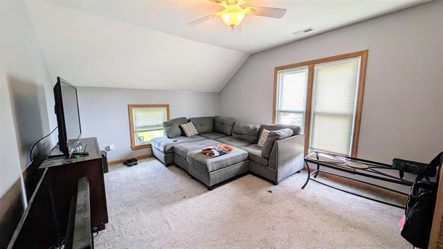 living area featuring plenty of natural light, carpet floors, vaulted ceiling, and a ceiling fan