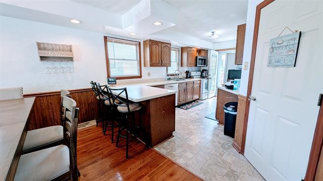 kitchen featuring white appliances, a kitchen bar, a peninsula, brown cabinetry, and plenty of natural light
