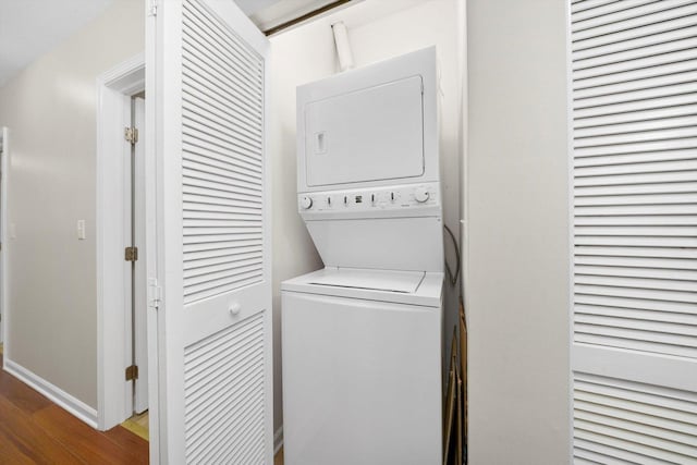 washroom with stacked washer / dryer, wood finished floors, and baseboards