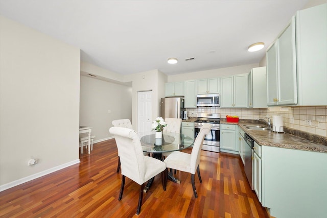kitchen with stainless steel appliances, dark countertops, backsplash, a sink, and dark wood-type flooring