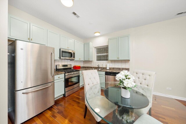 kitchen featuring stainless steel appliances, dark countertops, tasteful backsplash, dark wood finished floors, and a sink