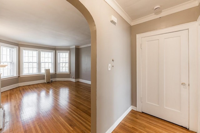 entrance foyer with arched walkways, light wood-style flooring, baseboards, and crown molding