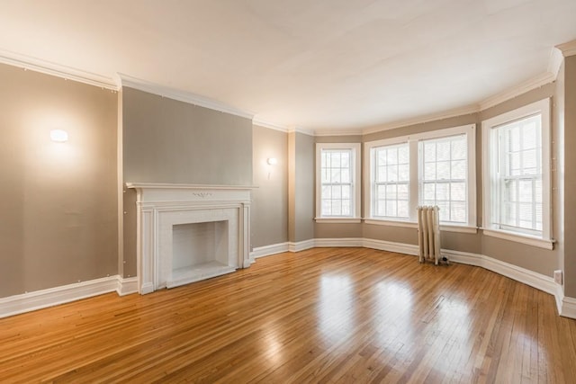 unfurnished living room featuring plenty of natural light, wood-type flooring, baseboards, a brick fireplace, and crown molding