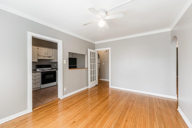 spare room featuring arched walkways, light wood-style flooring, ceiling fan, ornamental molding, and baseboards