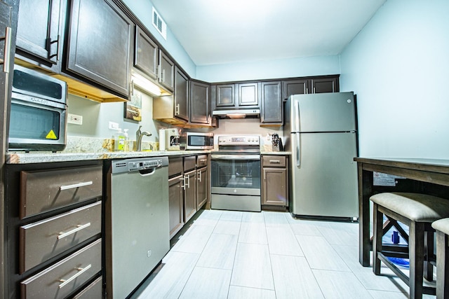 kitchen featuring appliances with stainless steel finishes, under cabinet range hood, light stone countertops, and a sink