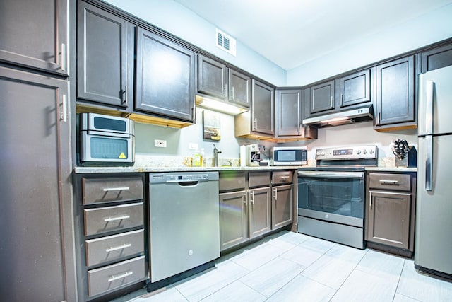 kitchen featuring appliances with stainless steel finishes, under cabinet range hood, light stone countertops, light tile patterned floors, and a sink