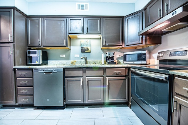 kitchen with stainless steel appliances, under cabinet range hood, a sink, light stone countertops, and light tile patterned floors