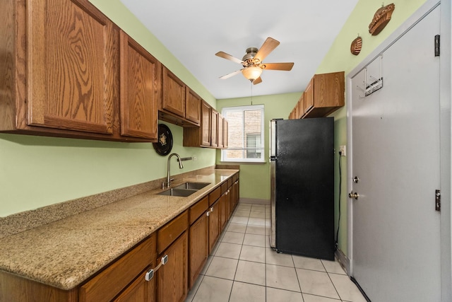 kitchen featuring freestanding refrigerator, a sink, ceiling fan, brown cabinetry, and light tile patterned floors