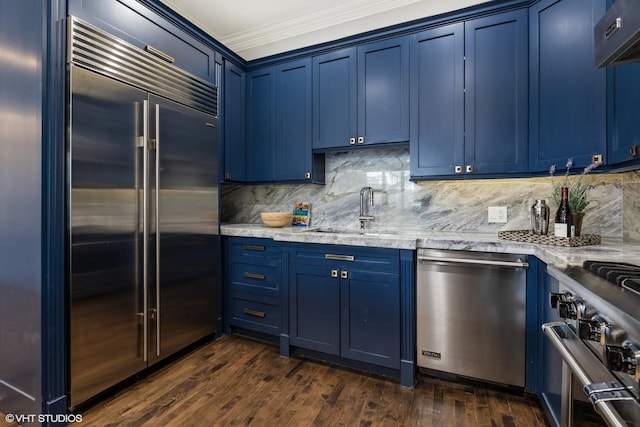 kitchen featuring premium appliances, blue cabinetry, a sink, ornamental molding, and dark wood-style flooring