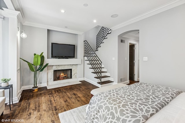 bedroom featuring wood finished floors, crown molding, arched walkways, a premium fireplace, and baseboards