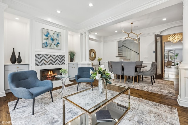 living area with dark wood-type flooring, a fireplace, stairway, decorative columns, and crown molding