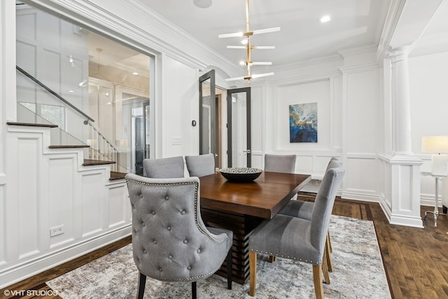 dining area featuring ornate columns, a decorative wall, dark wood-style flooring, ornamental molding, and stairway