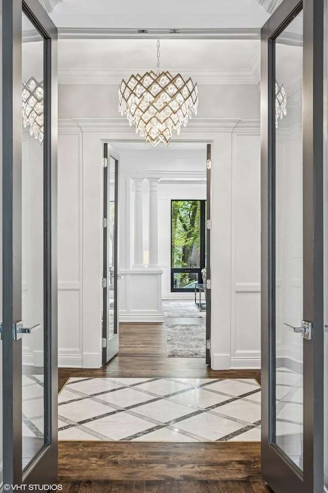 doorway to outside featuring wood-type flooring, inlaid floor details, a chandelier, a decorative wall, and ornamental molding