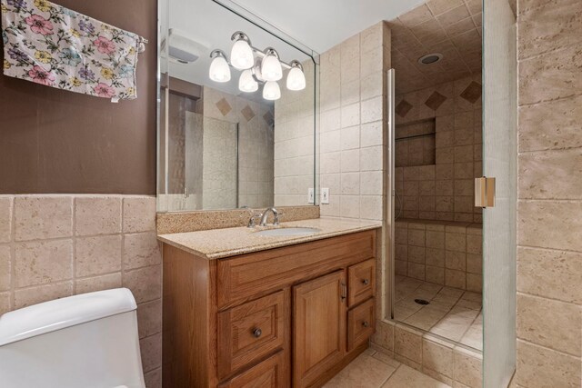 full bath featuring tile walls, a shower stall, vanity, toilet, and tile patterned floors