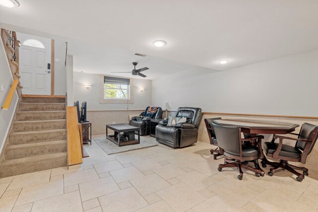 living area featuring ceiling fan, stairway, and wainscoting